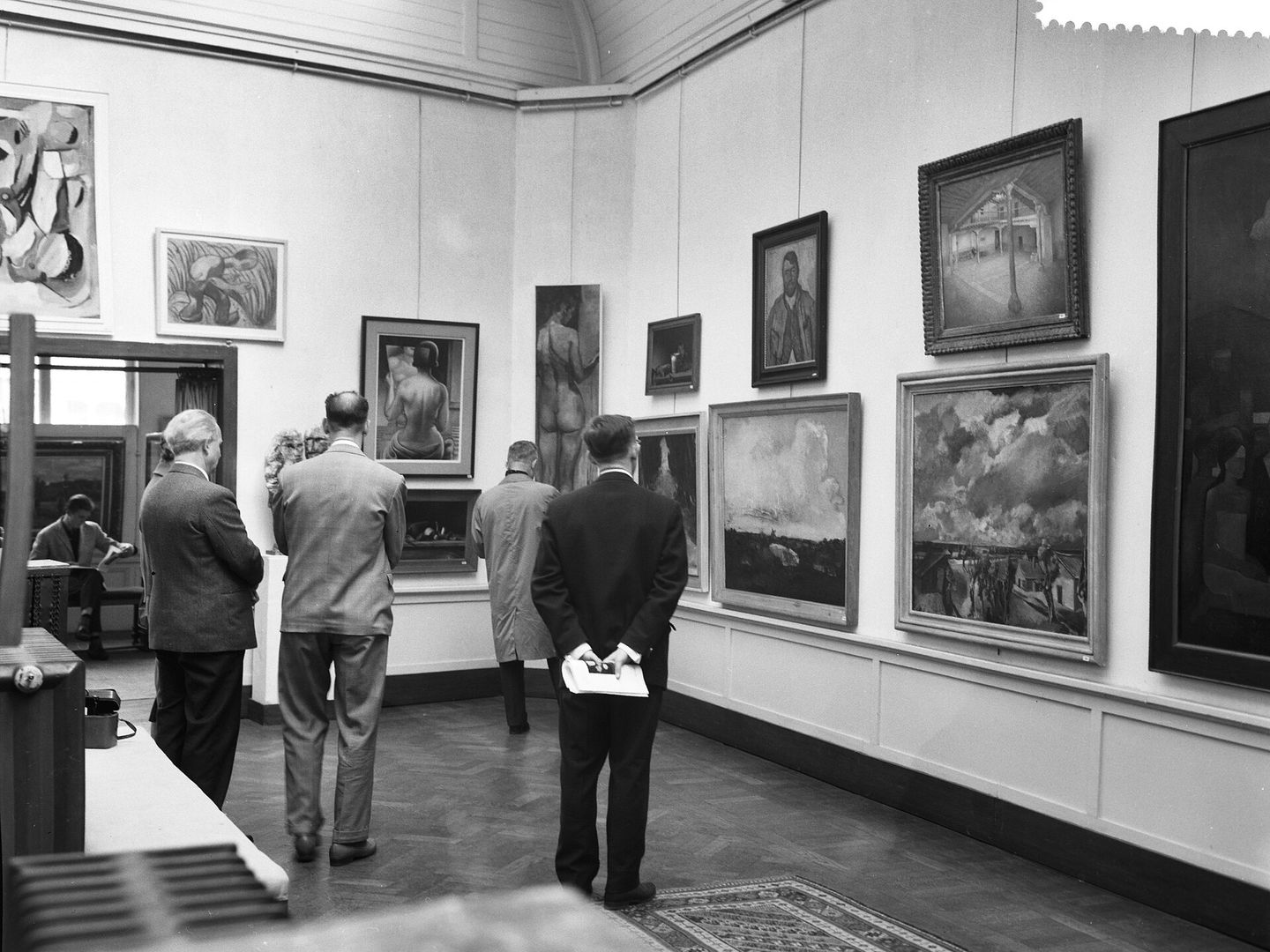 Bezoekers lopen langs schilderijen aan de wanden van een tentoonstellingszaal
