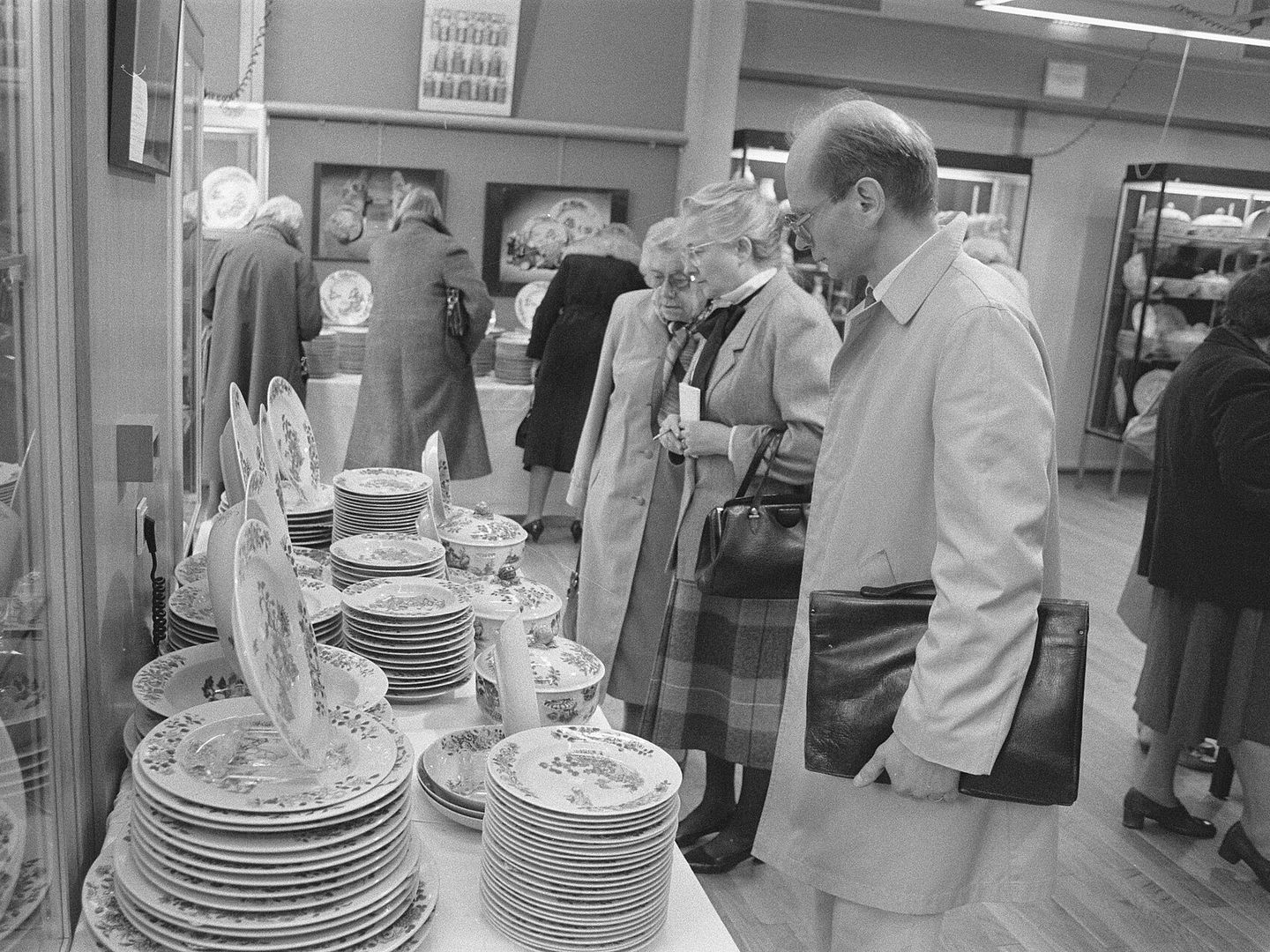 Bezoekers op een kijkdag bekijken stapels porseleinen borden en schalen op lange tafels