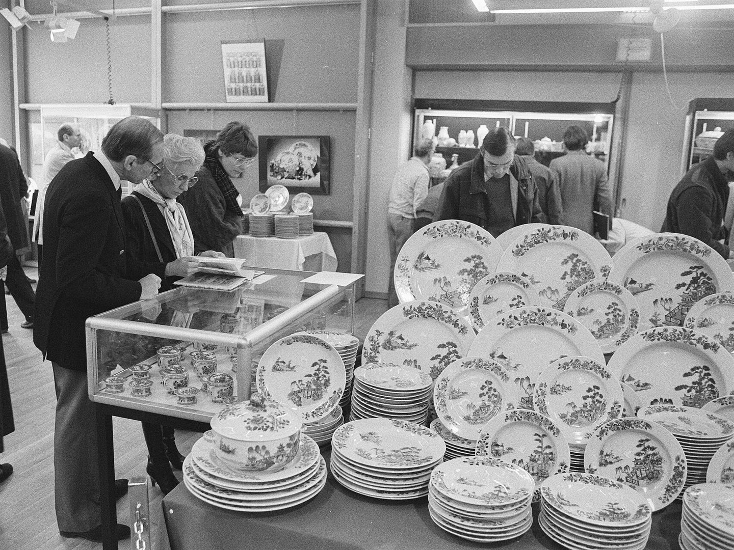 Kijkers buigen zich over een vitrine en tafels vol beschilderde borden tijdens een kijkdag