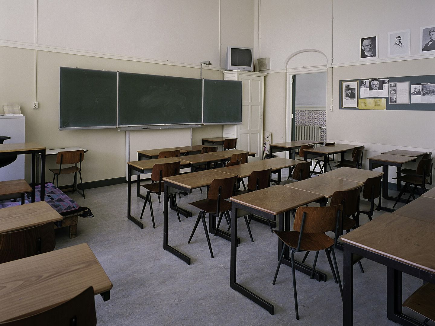 Klaslokaal met houten tafels en schoolstoelen op stalen poten voor een groen schoolbord