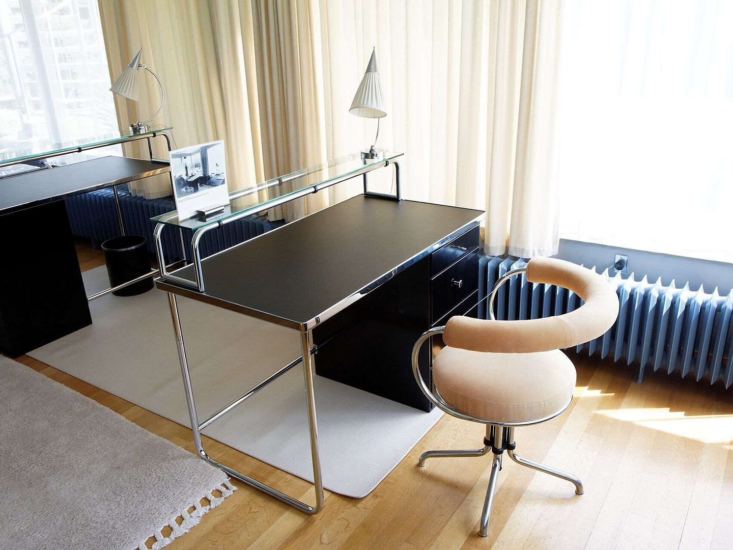 Bureau met een verchroomd stalen buisframe, een zwart blad en een ladenblok bij een raam