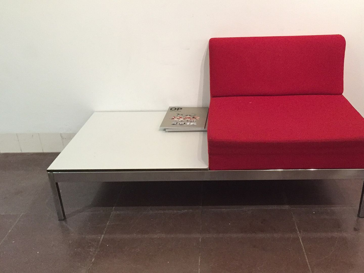 Een fauteuil met rode kussens en een verchroomd onderstel, met een wit tafelblad ernaast