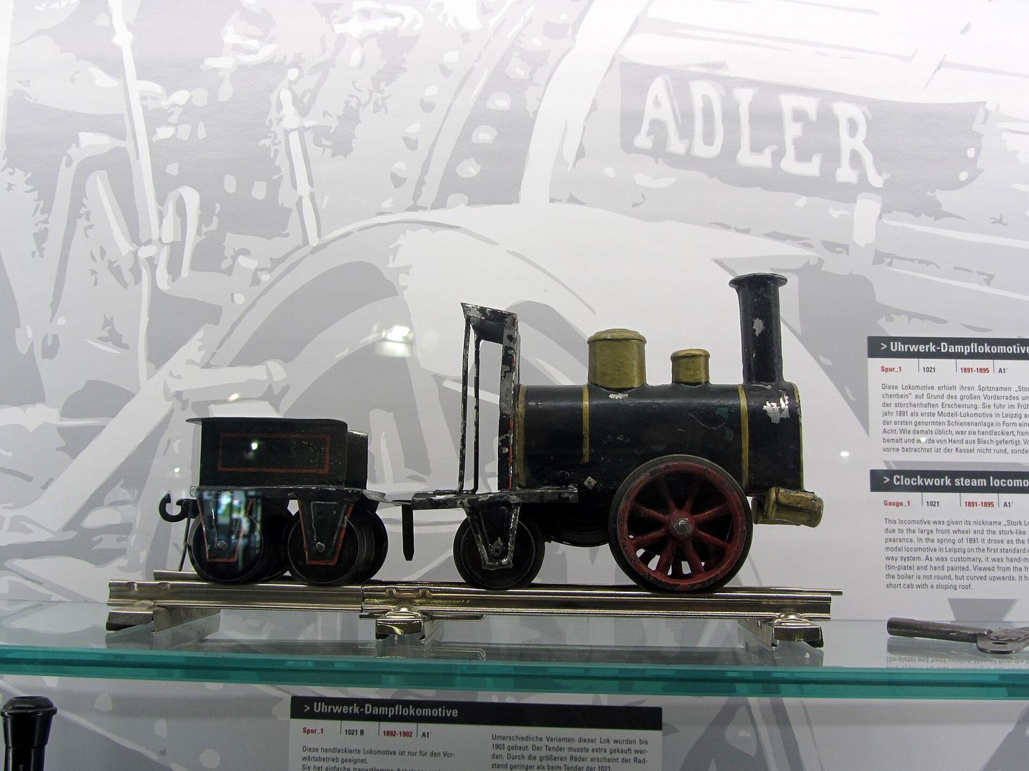 Zwarte blikken stoomlocomotief met groot rood voorwiel en tender in een museumvitrine