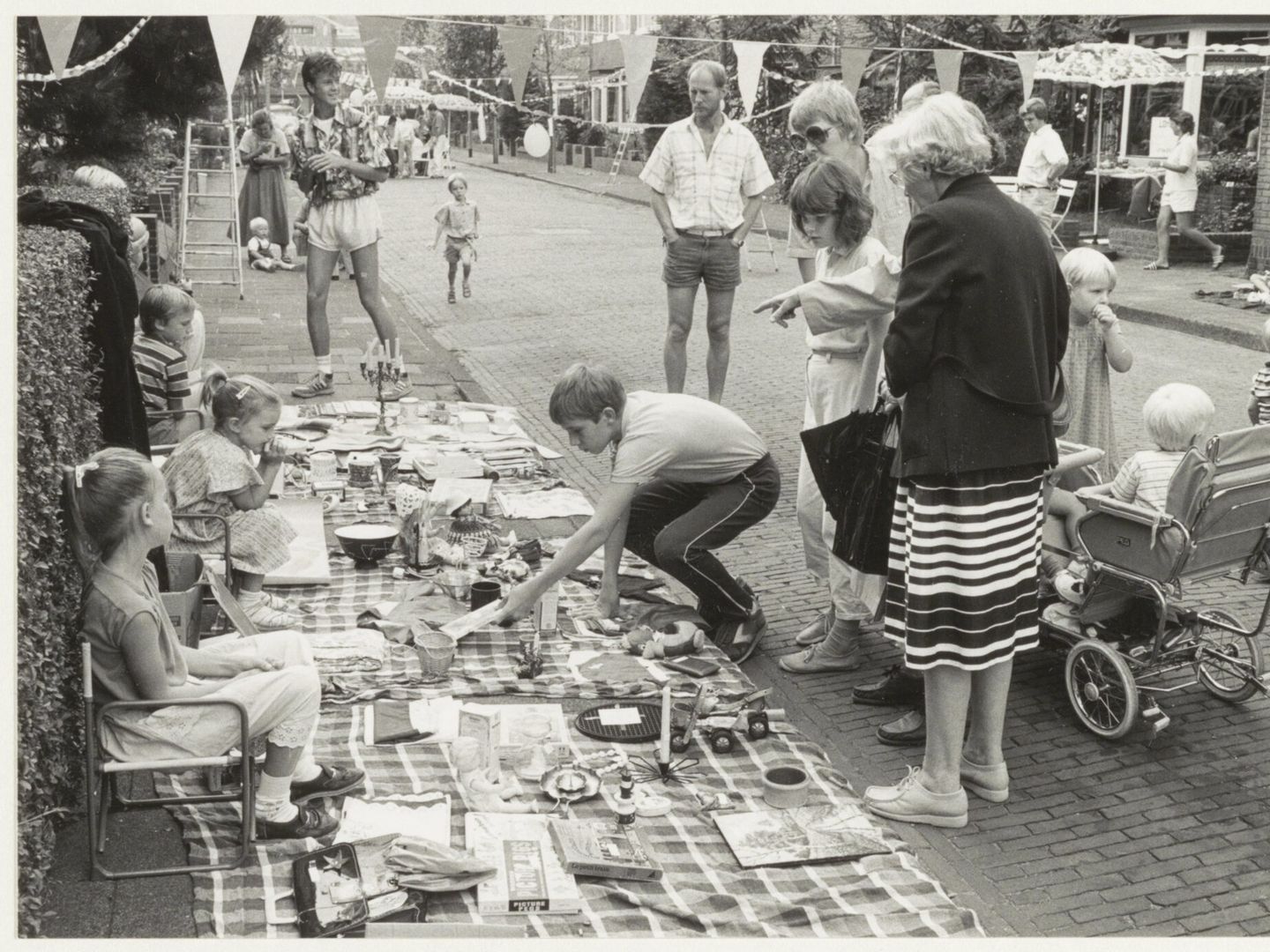 Kinderen en volwassenen bij kleden vol spullen op een rommelmarkt in de Dolfijnstraat