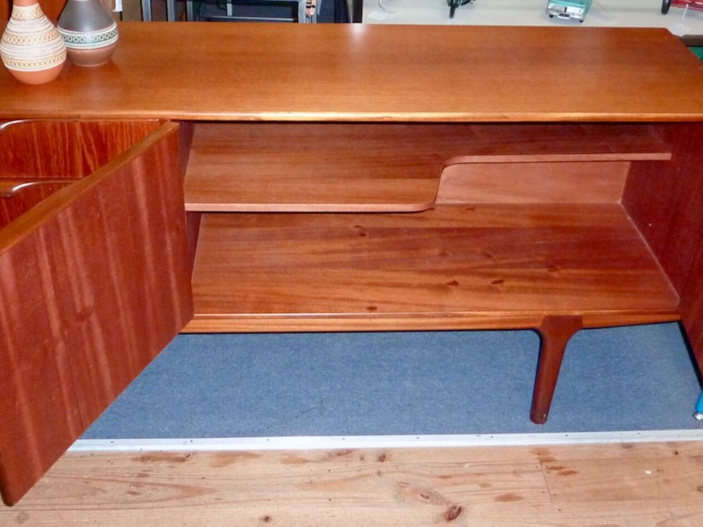 Teakhouten dressoir met twee geopende deuren, een binnenplank en drie laden links