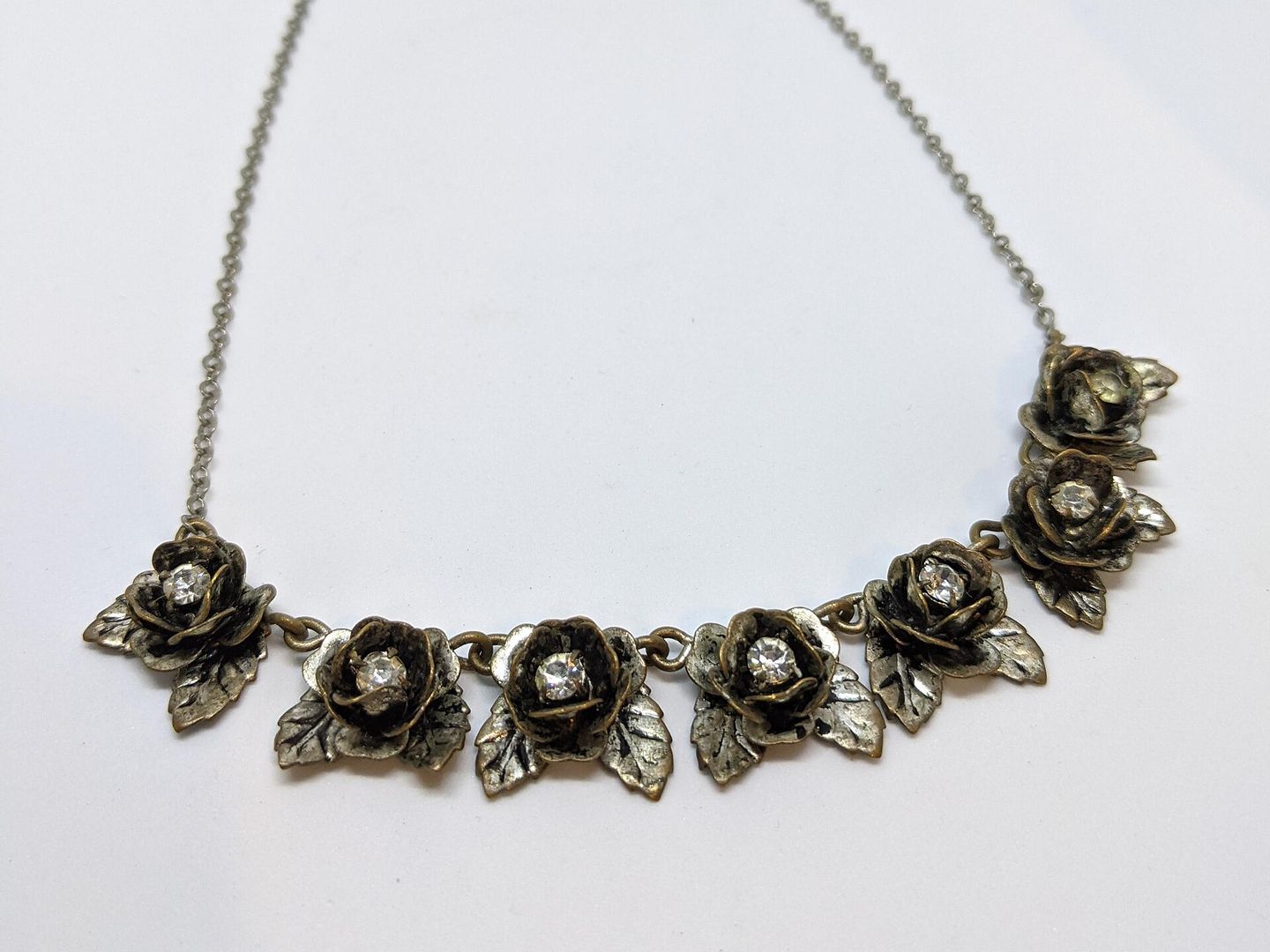 Ketting van donker metaal met een rij kleine rozen, elk met een glinsterend steentje in het hart