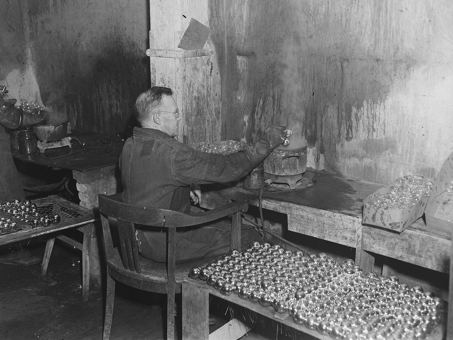Man aan een werkbank in een werkplaats met rijen verzilverde kerstballen