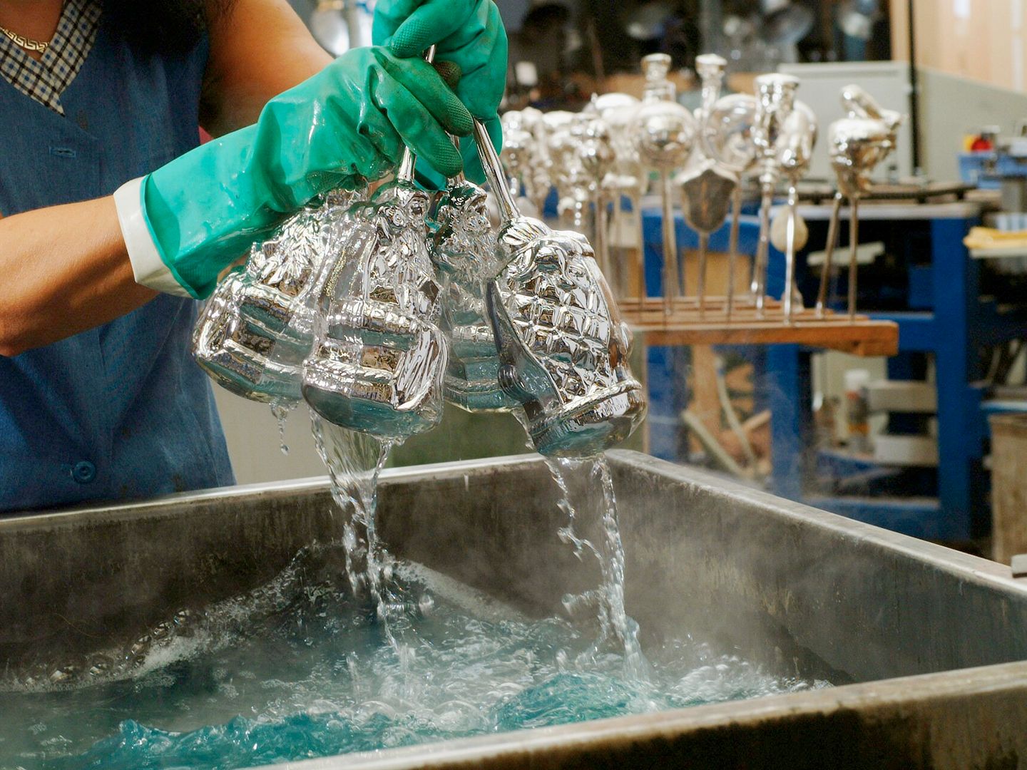 Handen in rubberen handschoenen schudden verzilverde glazen figuren in een bak heet water