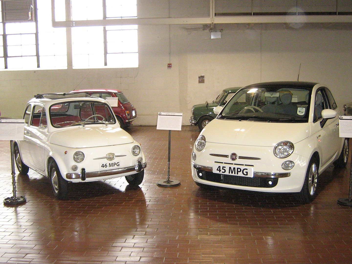 Een kleine witte Fiat 500 uit 1966 naast een grotere witte Fiat 500 uit 2008 in een museumzaal