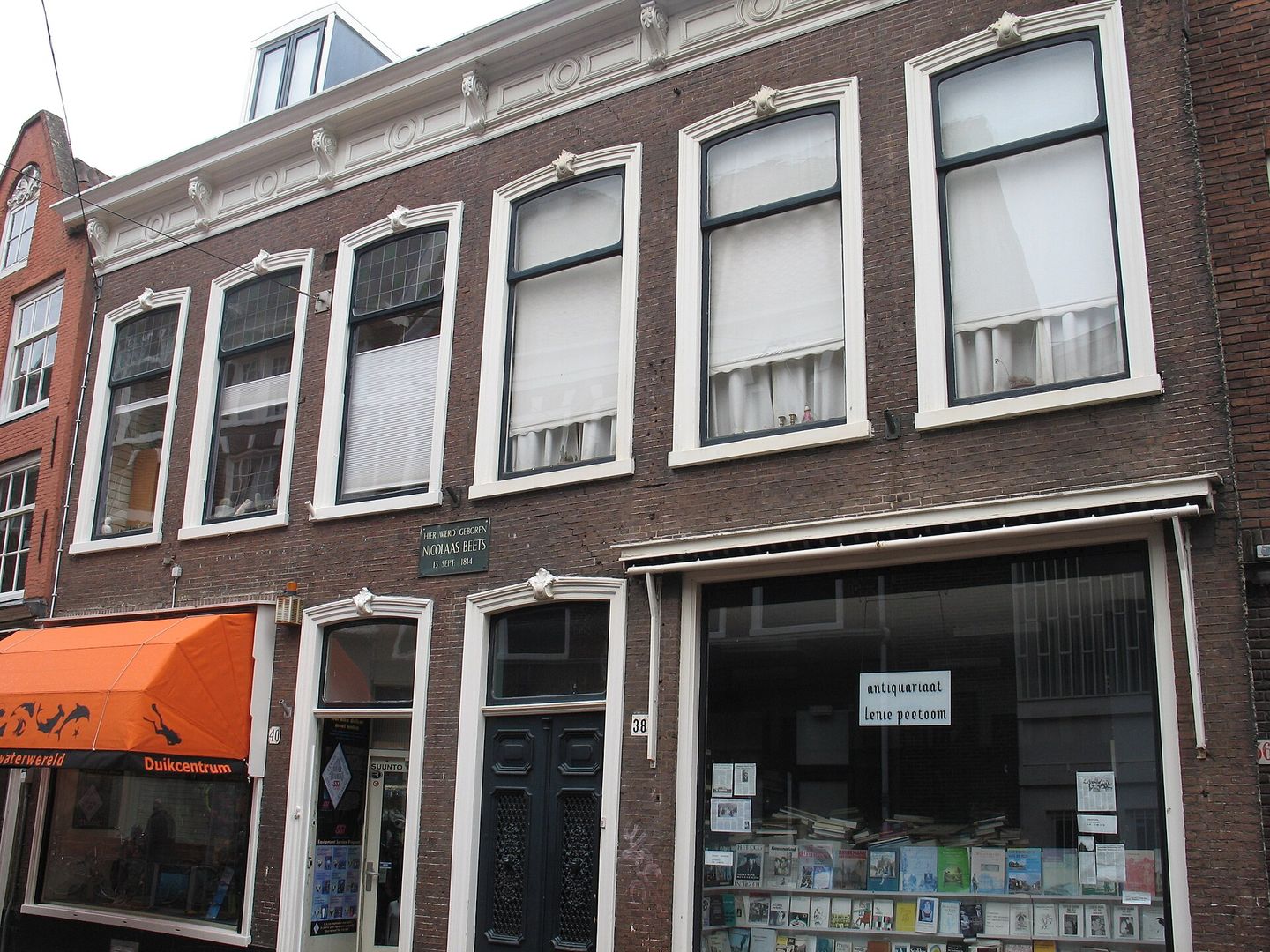 Bakstenen pand met witte kozijnen in de Koningstraat, met een antiquariaat op de begane grond