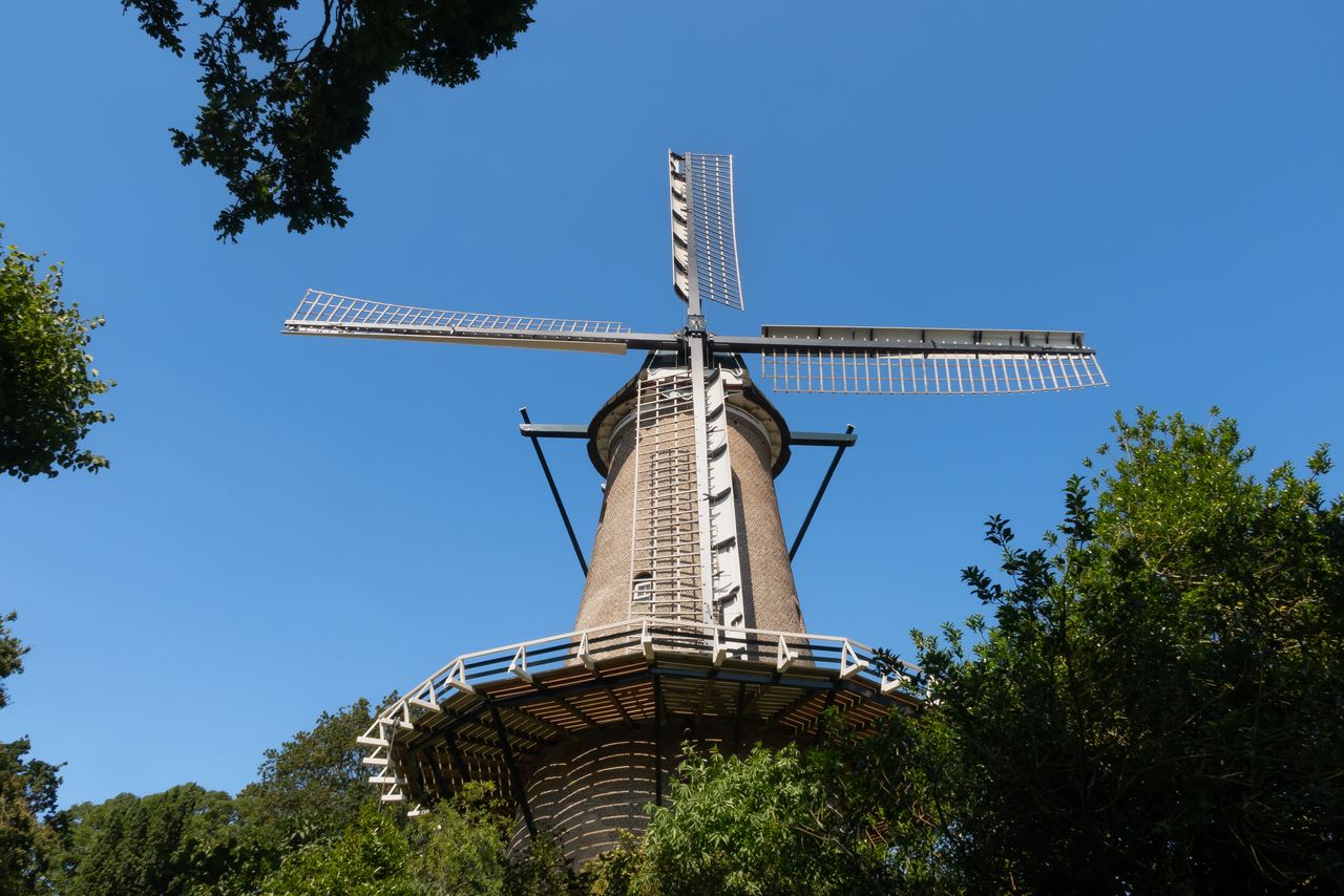 Stenen stellingmolen met witte wieken tegen een strakblauwe lucht, omringd door groen op het bolwerk