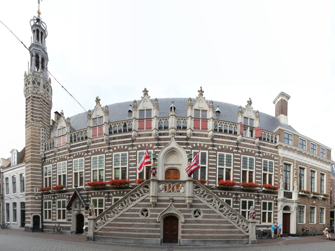 Laatgotisch stadhuis met gestreepte bakstenen gevel, bordestrap, rode bloembakken en slanke toren