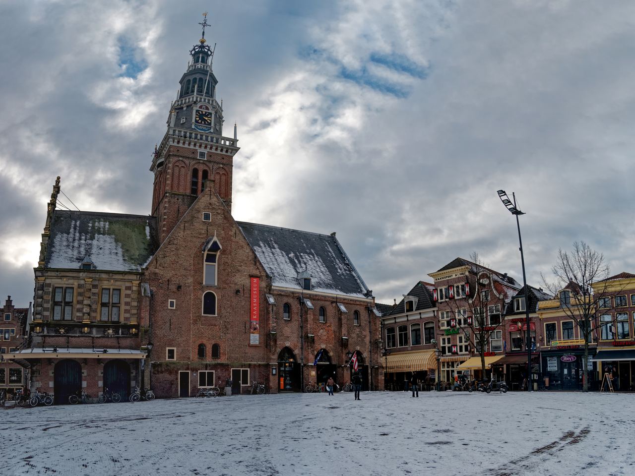 De bakstenen Waag met klokkentoren op het besneeuwde Waagplein, rechts een rij oude gevels met luifels