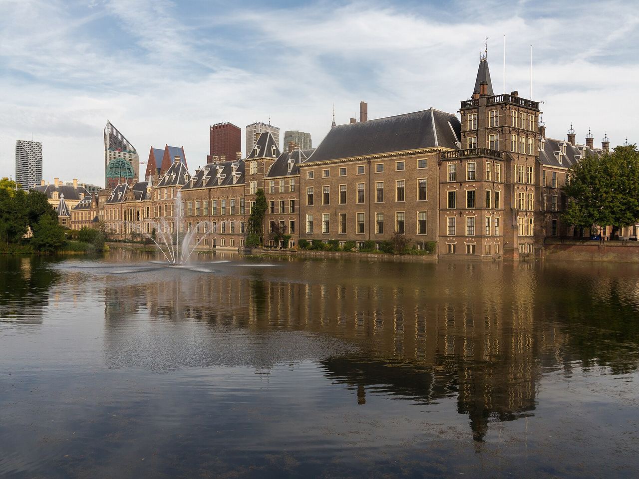 Het Binnenhof met de Ridderzaal en torentjes aan de Hofvijver, gespiegeld in het water met een fontein op de voorgrond