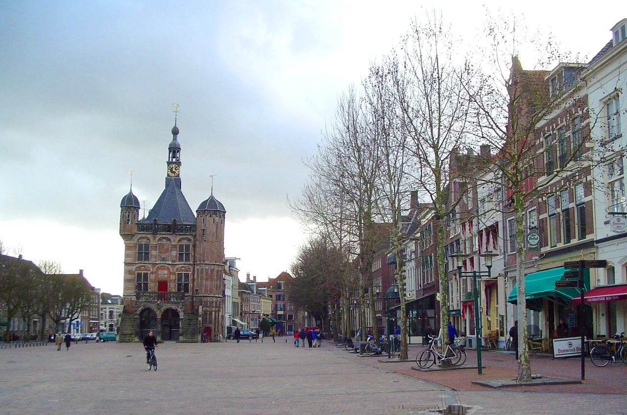 De laatgotische Waag met traptoren en spitstorentjes op de brede Brink, met bomen en gevels langs het plein