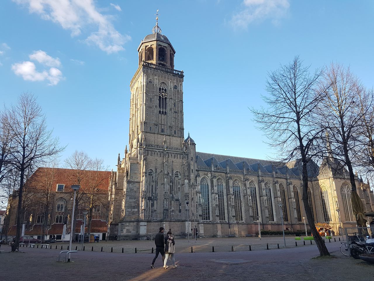 De Lebuinuskerk met hoge toren aan het Grote Kerkhof, met kale bomen en links het restant van de Mariakerk
