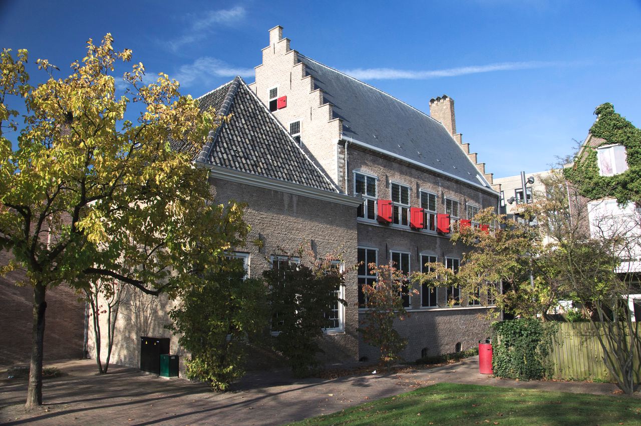 Het kloostergebouw van Het Hof met trapgevel en rode luiken, gezien vanuit de kloostertuin