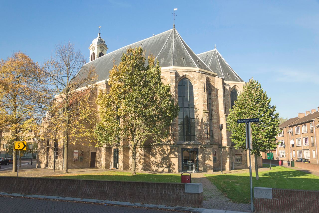 De gotische Nieuwkerk met klokkentorentje, omringd door bomen en een grasveld