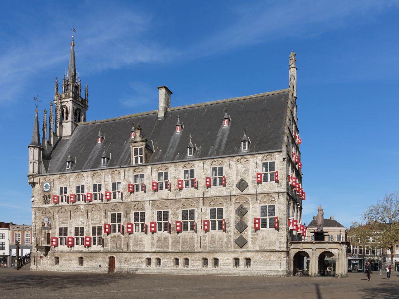 Het gotische stadhuis van Gouda met rood-witte luiken, gezien over de lege Markt onder een blauwe lucht