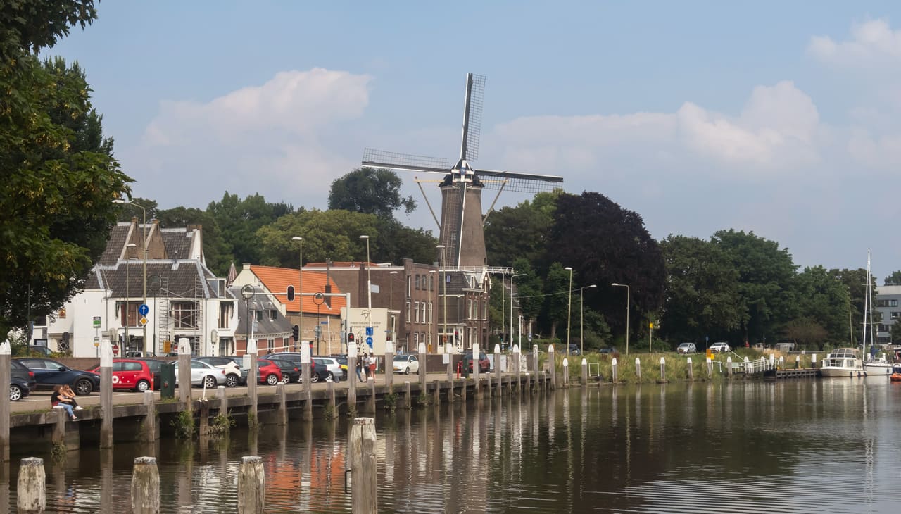 Molen 't Slot boven de huizen langs het water, met een kade met geparkeerde auto's op de voorgrond