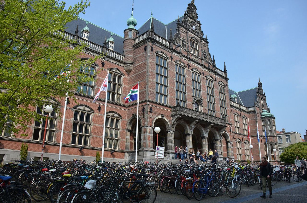 Het bakstenen Academiegebouw met torentjes en vlaggen, met rijen fietsen op het plein ervoor