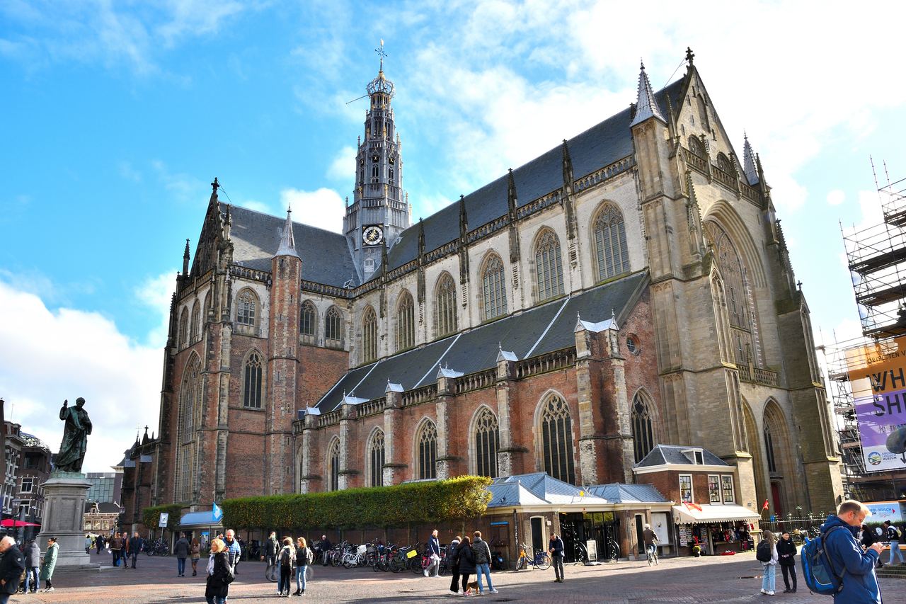 De Grote of Sint-Bavokerk met hoge vieringtoren aan de Grote Markt, met het standbeeld van Laurens Janszoon Coster links