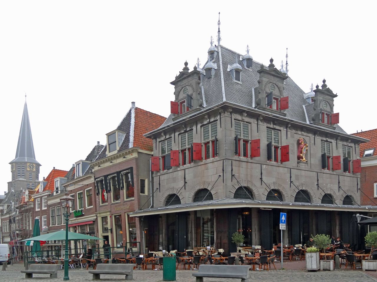 Het waaggebouw met rode luiken op de Roode Steen, met terrassen ervoor en links de toren van de Grote Kerk