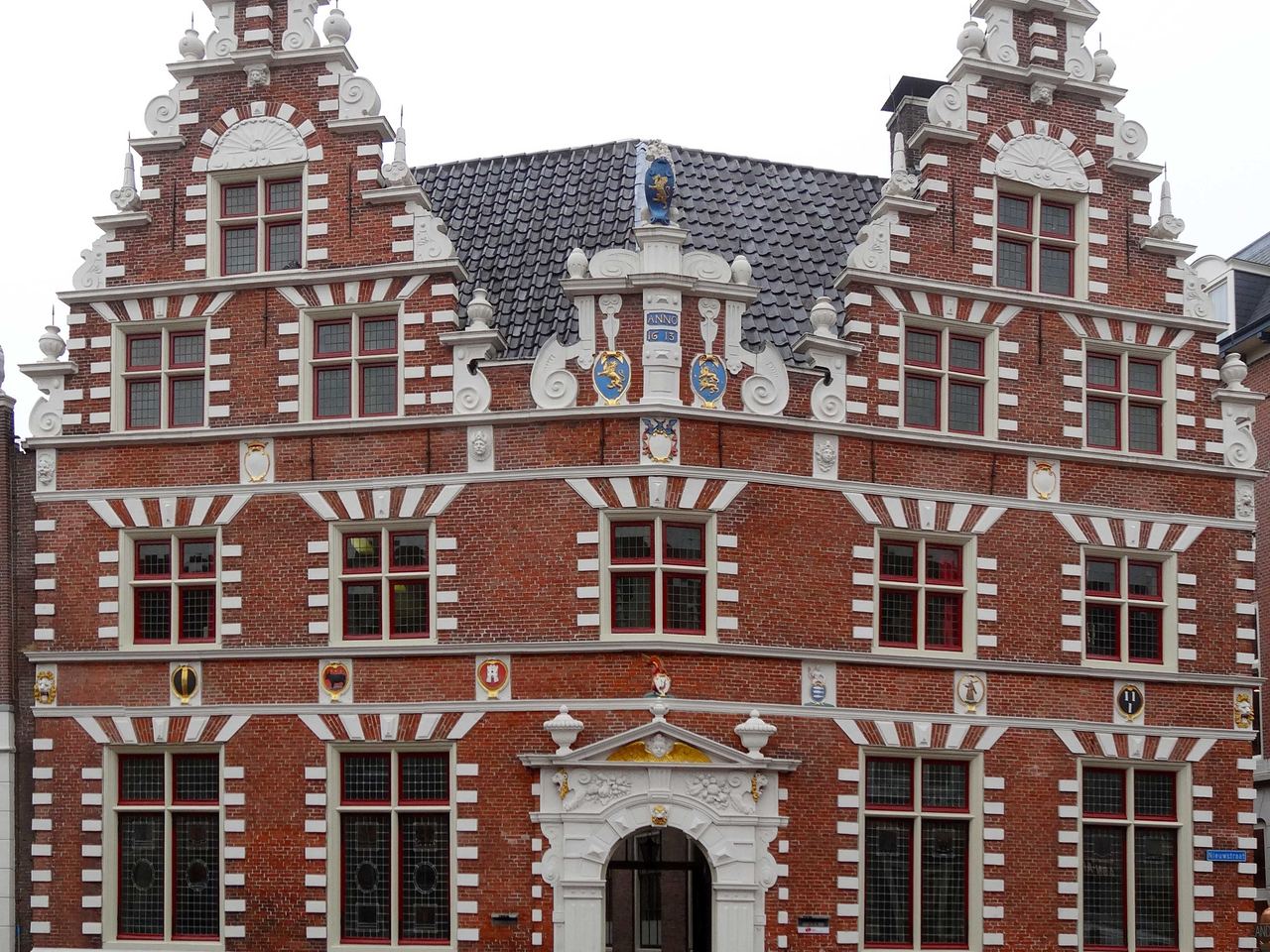 Rode bakstenen gevel met twee trapgevels en witte versieringen aan de Nieuwstraat