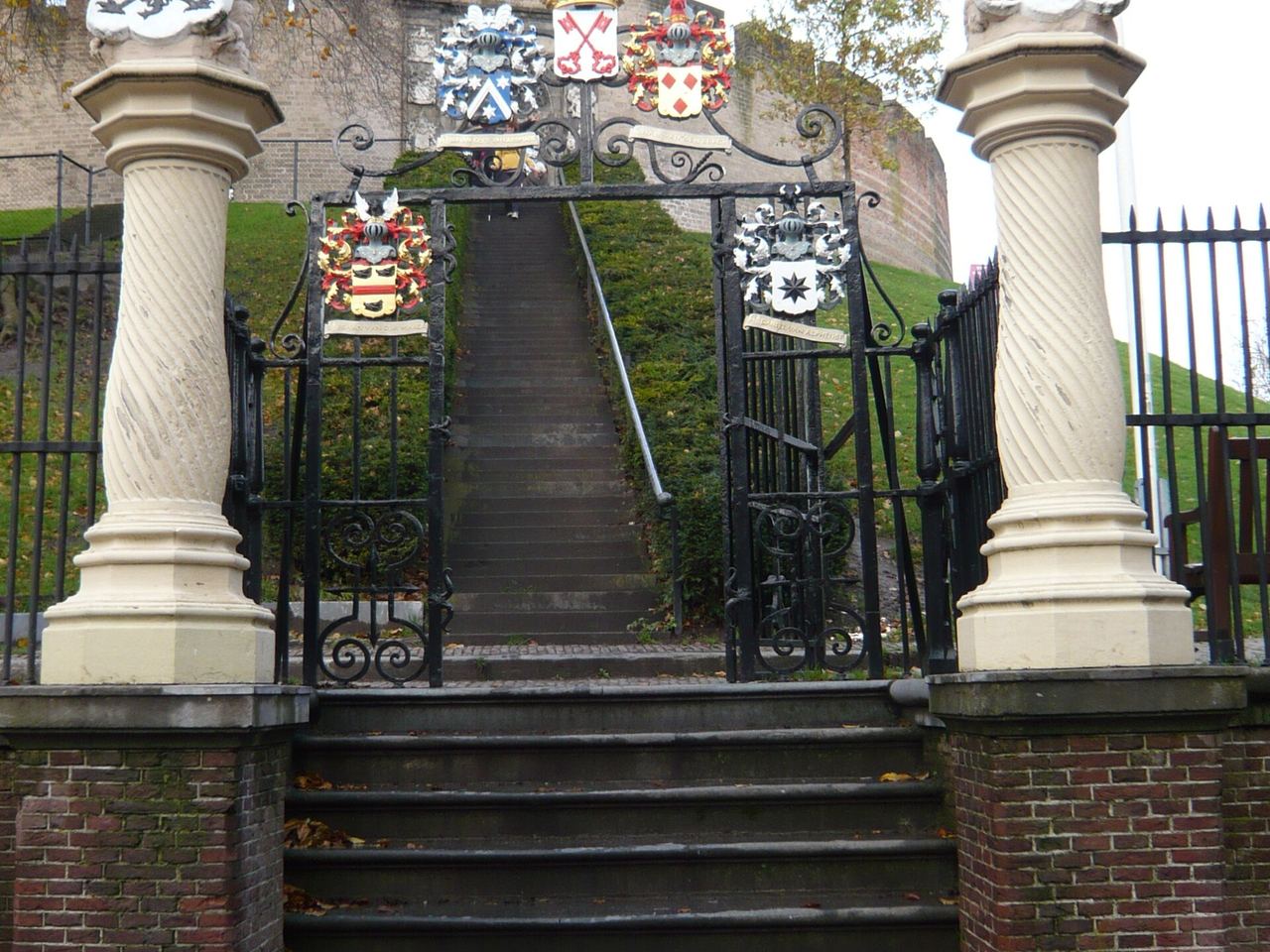 De smeedijzeren poort met wapenschilden en twee leeuwen op zuilen, met een trap naar de burchtheuvel