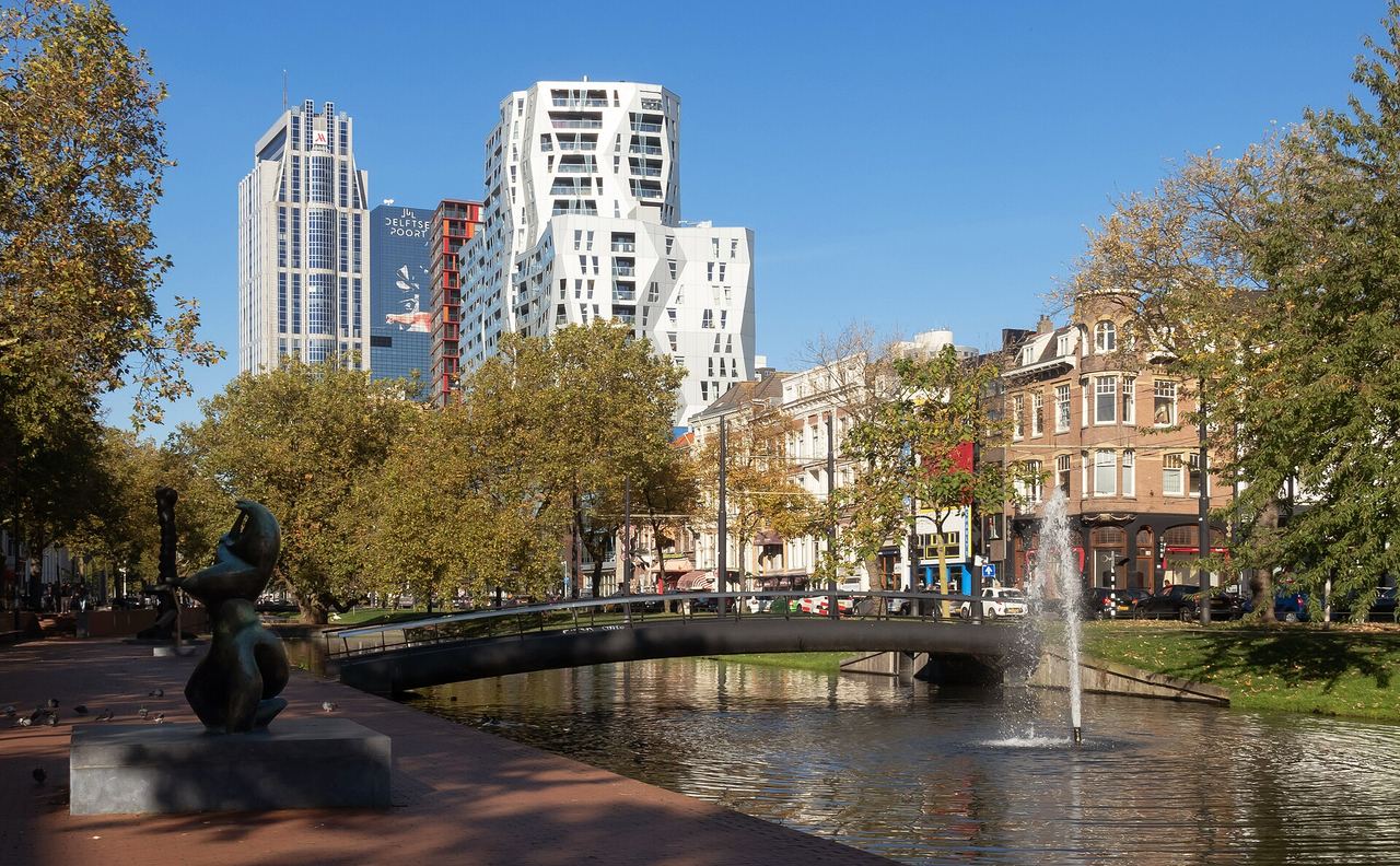 De Westersingel met een bronzen beeld aan het water, een fontein, een boogbrug en hoge torens achter de bomen