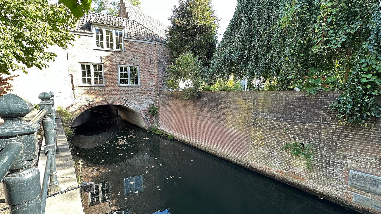 Het water van de Binnendieze tussen bakstenen muren, met een overkluizing onder de huizen