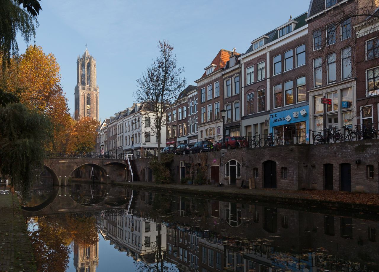 De Domtoren boven de Oudegracht, met grachtenpanden en een brug die in het stille water weerspiegelen