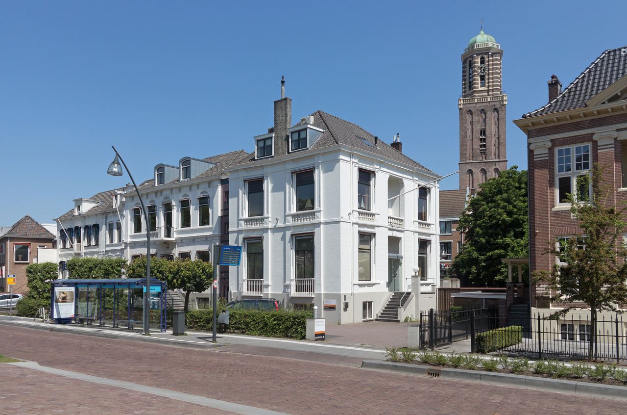 De Peperbus boven witte en bakstenen herenhuizen aan een brede straat met een bushokje