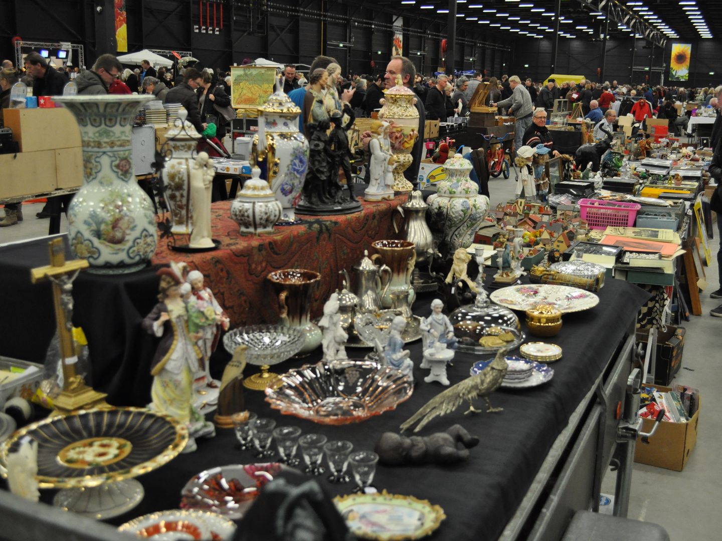 Kramen met porselein, vazen en beeldjes in de hal van Expo Assen, met bezoekers tussen de tafels
