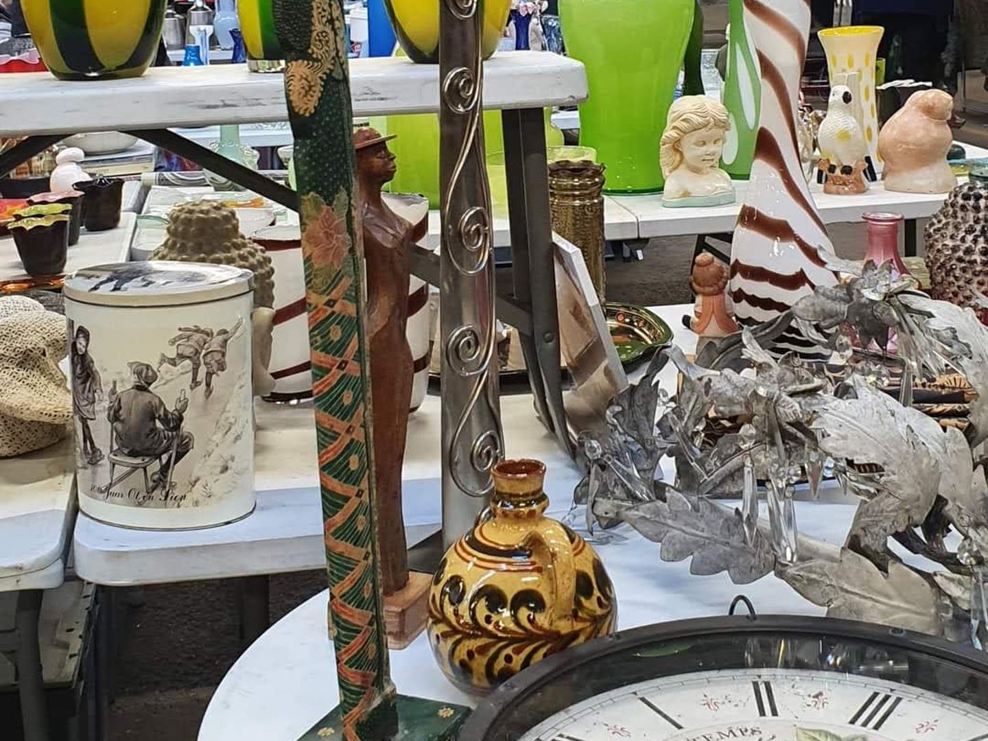 Glazen vazen in geel en groen, beeldjes en een oude klok op een kraam van de vlooienmarkt in de Flowerdome