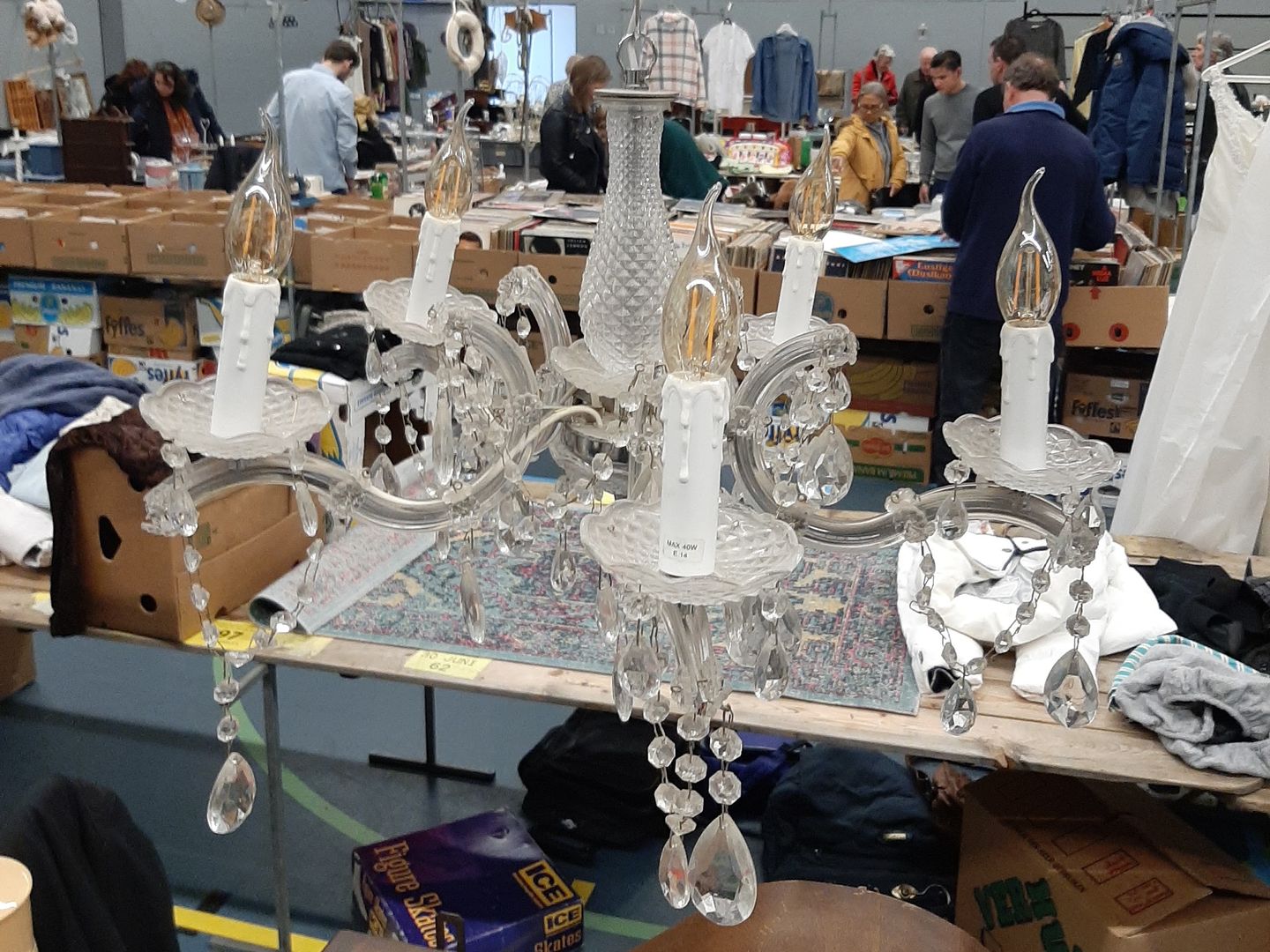 Kristallen kroonluchter boven een kraam op de snuffelmarkt in de Dudok Arena, met bakken platen erachter
