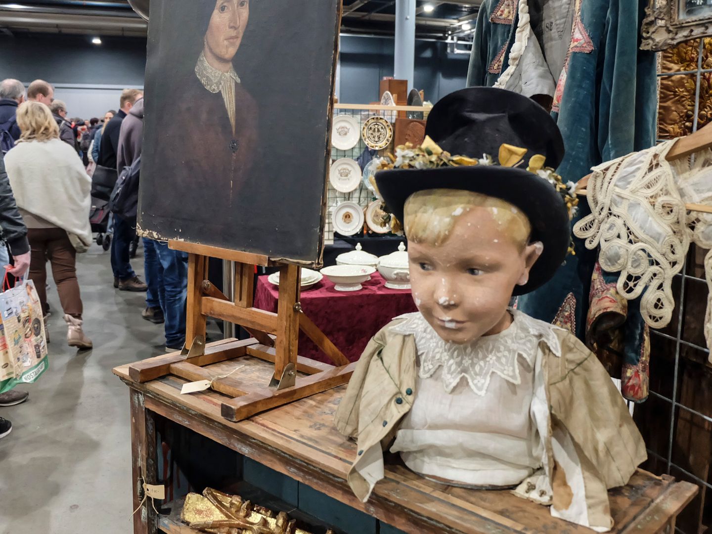 Kraam met curiosa in de Brabanthallen: een geschilderd portret op een ezel en een pop met hoge hoed