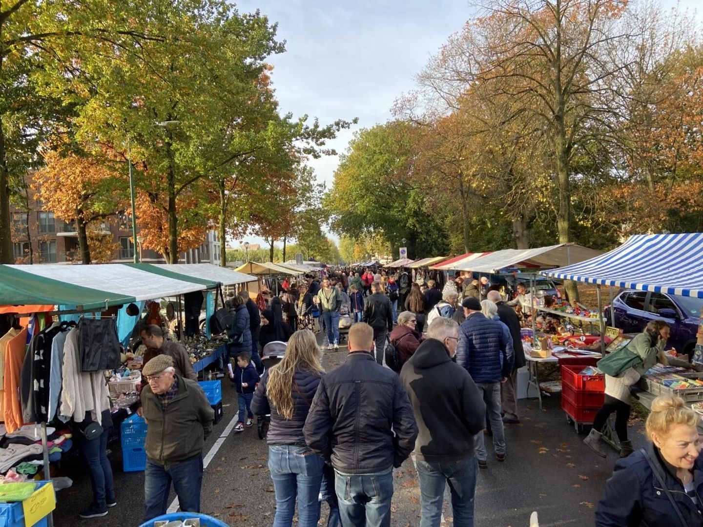 Drukke straatmarkt onder herfstbomen in het centrum van Soesterberg, met kramen vol kleding en huisraad