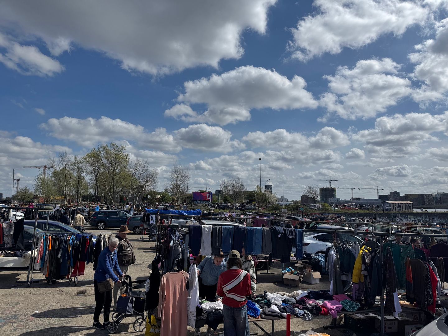 Lange rijen kledingrekken en bezoekers op de buitenmarkt van de IJ-Hallen op de NDSM-werf
