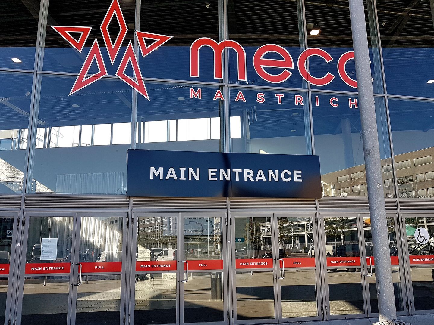 De glazen hoofdingang van het MECC in Maastricht met de naam van het congrescentrum erboven