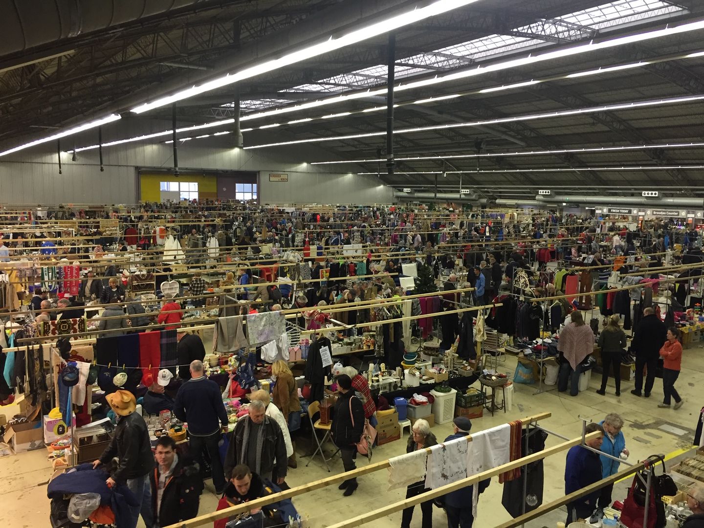 Lange rijen kramen en kledingrekken met bezoekers in Hangar 11 tijdens een eerdere vlooienmarkt