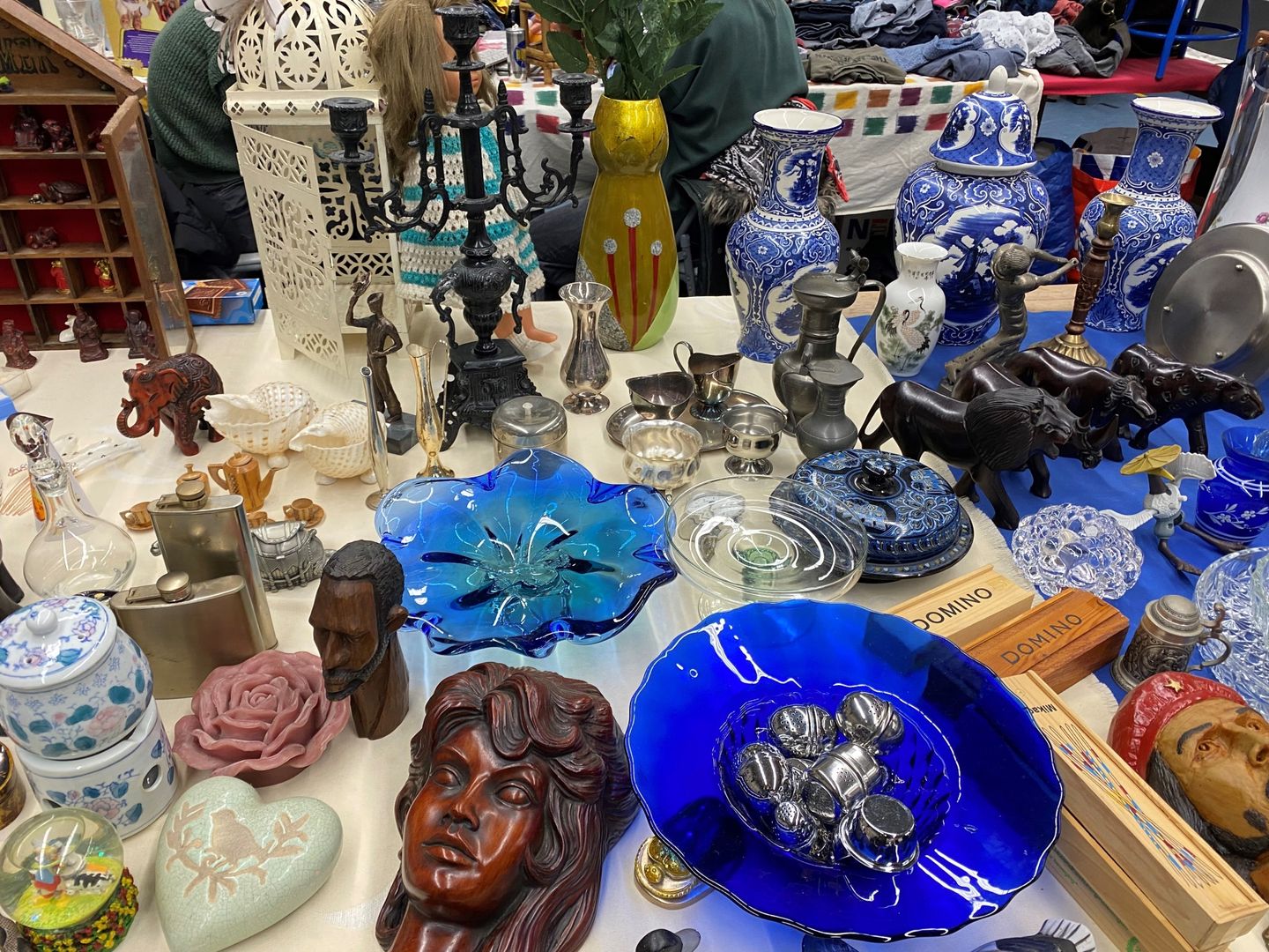 Kraam met blauwe glazen schalen, Delfts aardewerk, koperen kandelaars en houten beeldjes