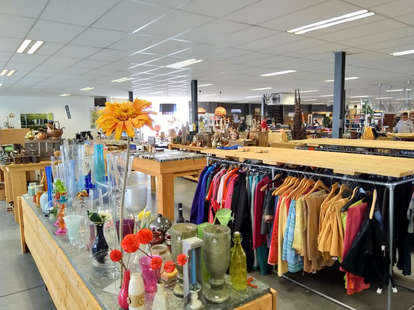 Winkelvloer van 2Switch met glazen vazen, kledingrekken en houten tafels