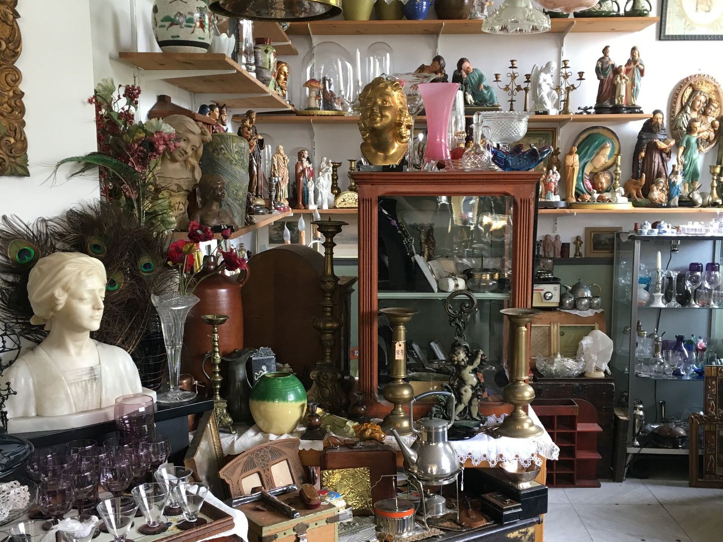 Interieur van Antiek Déjà Vu met wandplanken vol beelden, kandelaars, een vogelkooi en antieke kasten
