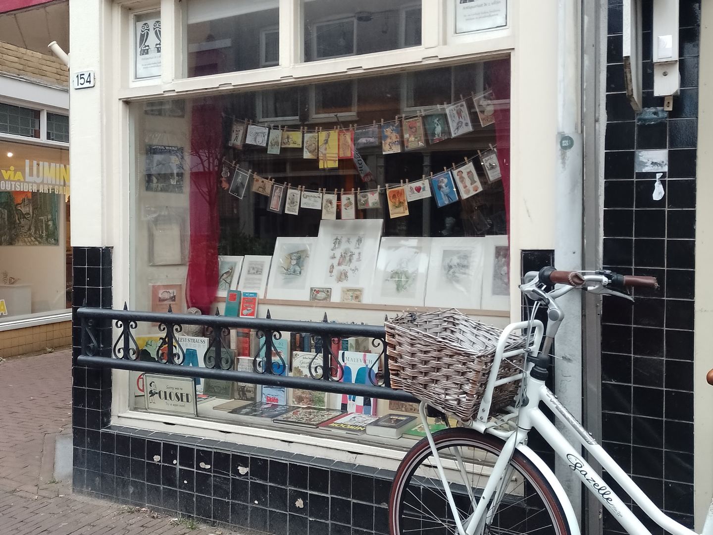Gevel van De 2 uiltjes boeken en prenten met prenten in de etalage en een fiets ervoor