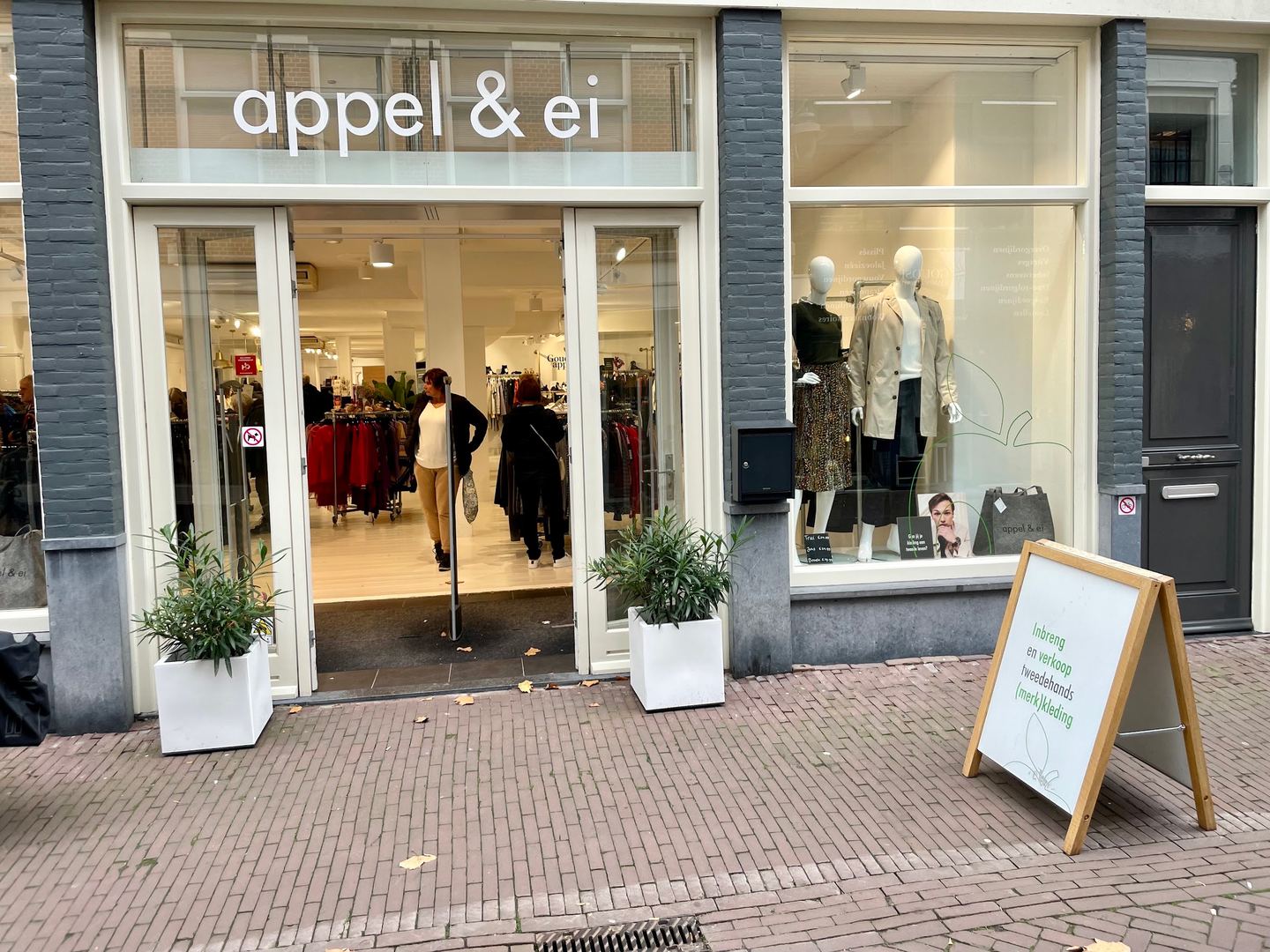 Winkelpui van Appel & Ei met naam boven de glazen deuren, etalagepoppen en een stoepbord
