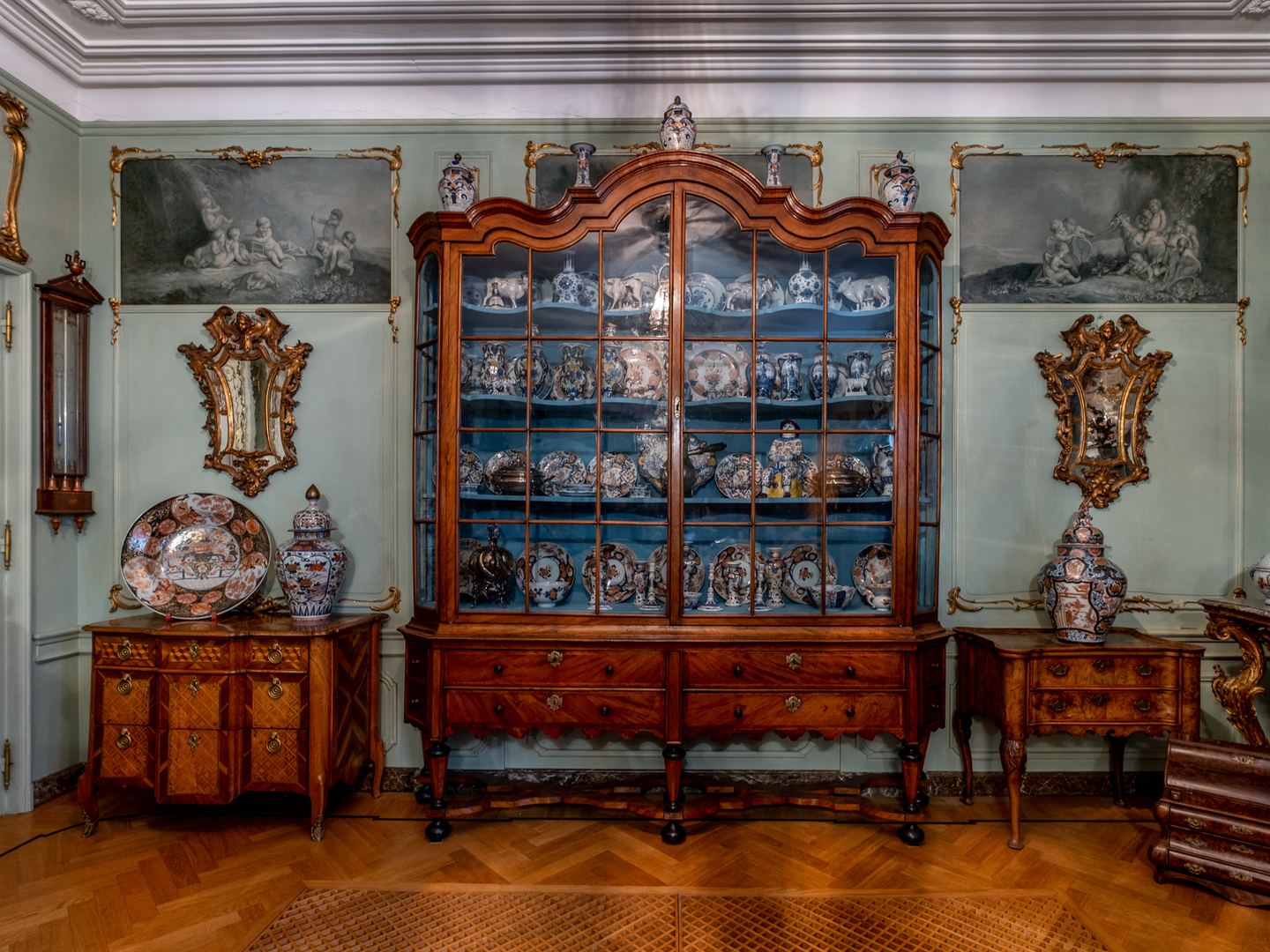 Stijlkamer van Berden Antiquairs met een vitrinekast vol porselein, antieke meubels en spiegels
