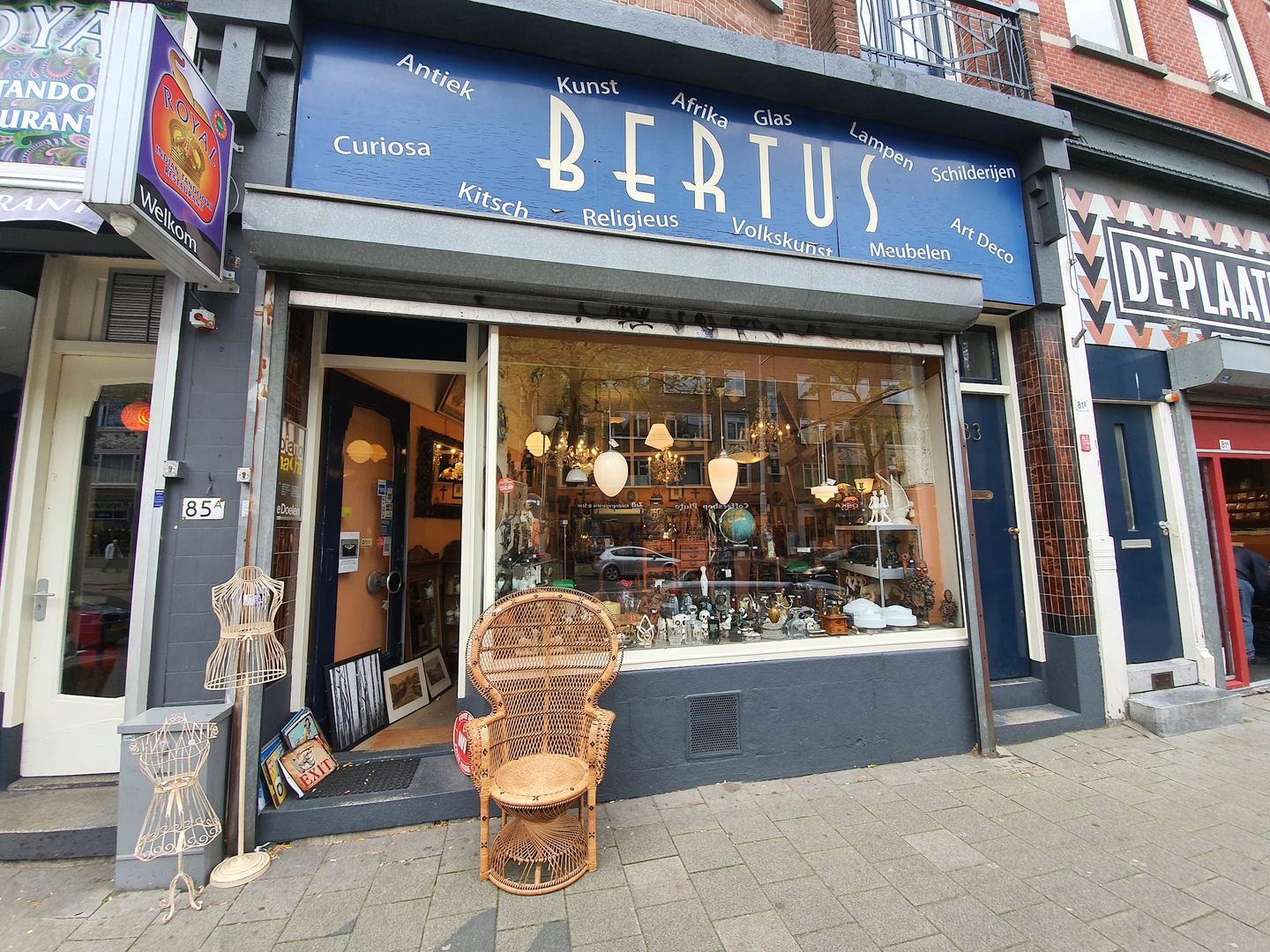Winkelpui van Bertus Antiek en Curiosa met blauw naambord en een etalage vol lampen en curiosa