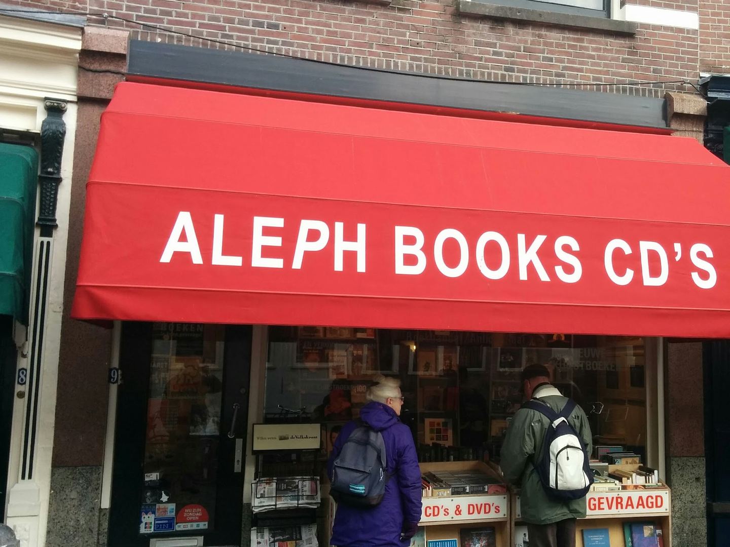 Gevel van Boekhandel-Antiquariaat Aleph met rode luifel en boekenbakken voor de deur
