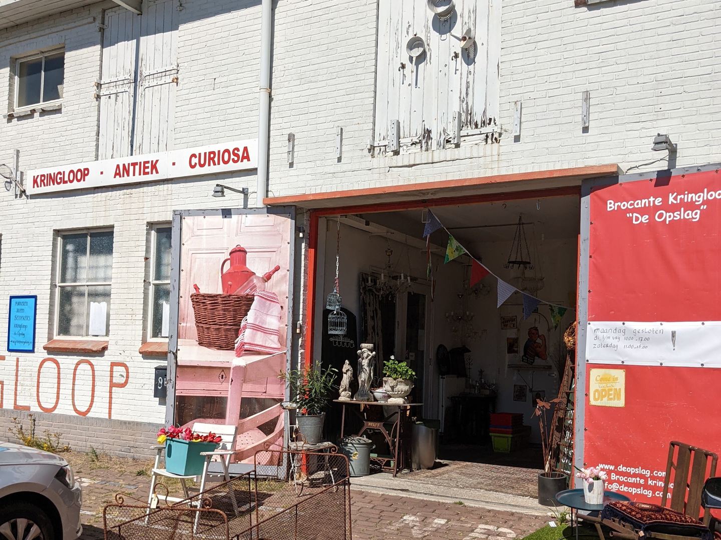 Ingang van Brocante Kringloop De Opslag met spandoek en brocante buiten